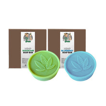 Load image into Gallery viewer, Two round soap bars from Green Apron are pictured in front of their respective brown packages. One soap bar is green, labeled "Lady Green Hemp Soap Bar," and the other is blue, also labeled "Lady Green Hemp Soap Bar." Both soaps feature a leaf imprint on top.